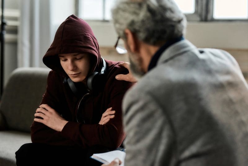 Therapist using CBT to support depressed teenage boy during appointment
